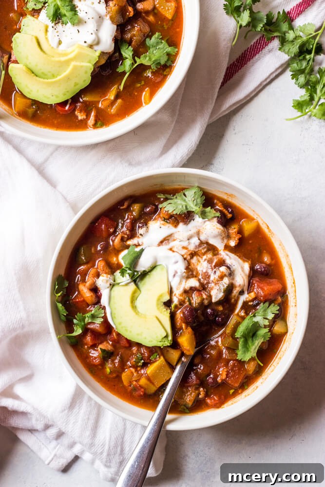 Spicy Sunshine Stew 2 A steaming bowl of vibrant summer vegetable chili, garnished with fresh cilantro and a dollop of sour cream, resting on a rustic wooden surface.