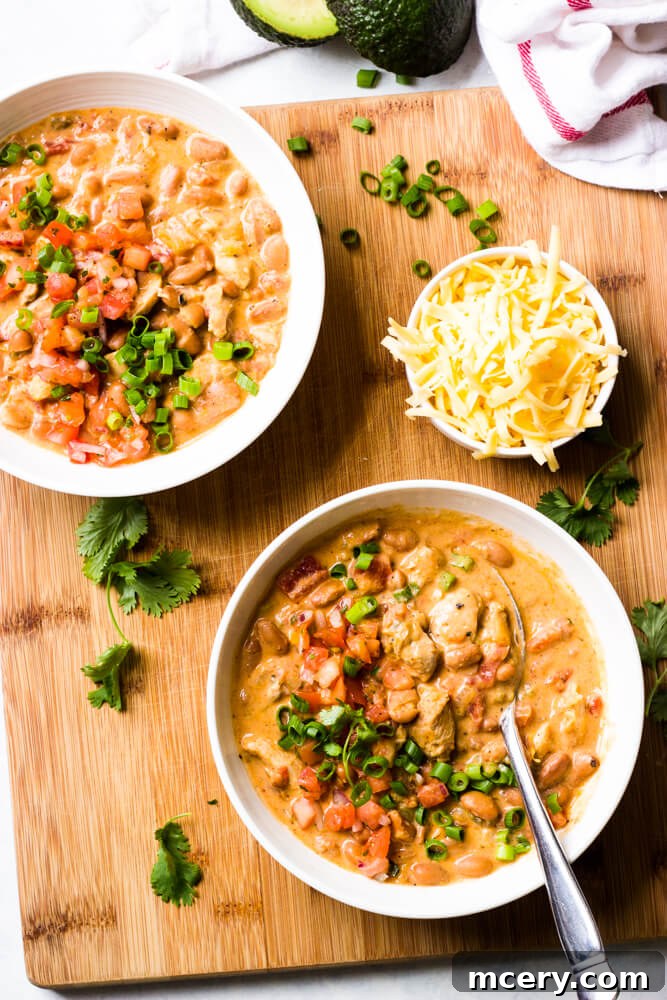 Whip Up the Ultimate Chicken Chili 2 Overhead view of creamy chicken chili in white bowls with side of shredded cheese