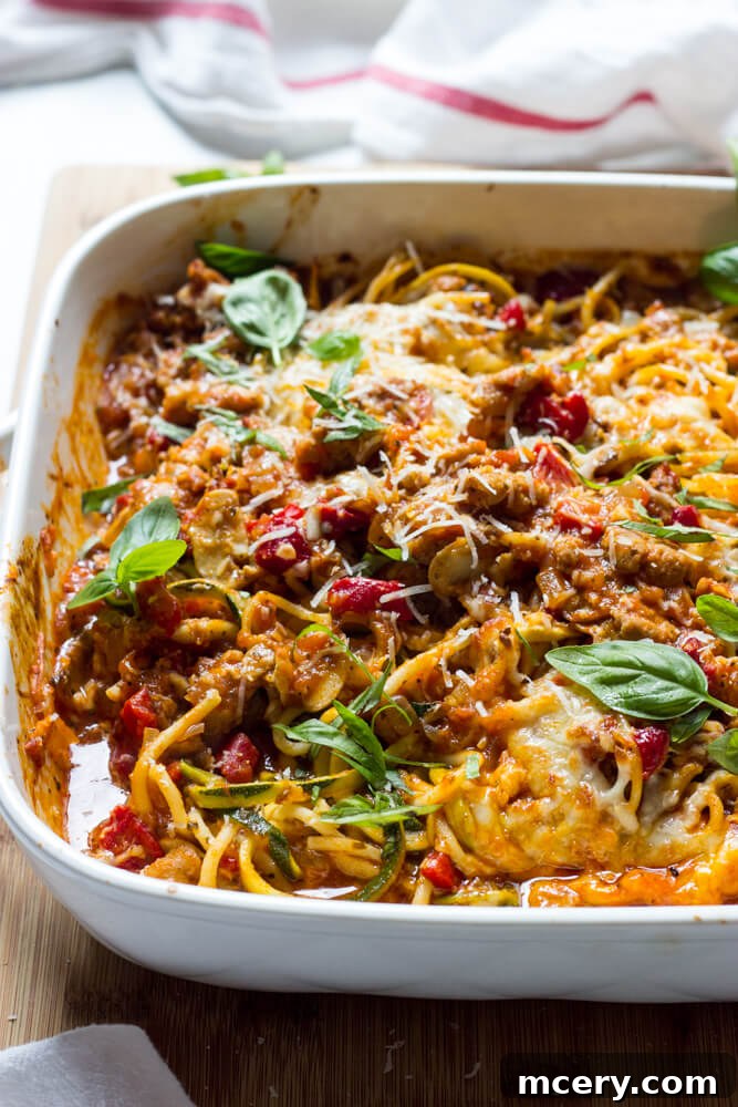 Side close-up of a beautifully baked zucchini and spaghetti casserole in a white dish, showcasing its cheesy topping and rich layers.