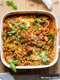 Overhead view of spaghetti and zucchini bake in white casserole dish, garnished with fresh basil.