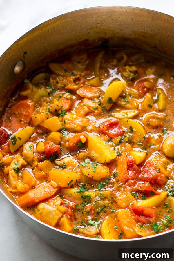 Hearty Butternut Chicken Stew 7 An overhead shot of hearty chicken stew with butternut squash in a dark red Dutch oven, garnished with fresh herbs, indicating it's ready to be served.