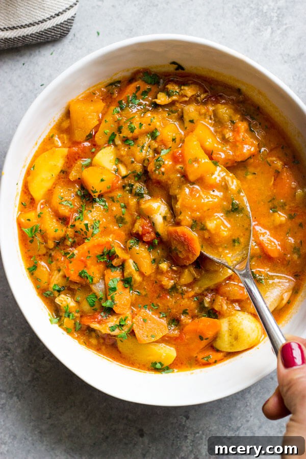 Hearty Butternut Chicken Stew 8 An overhead view of a single serving of chicken stew with butternut squash in a white bowl, with a spoon positioned on the side, ready to be eaten.
