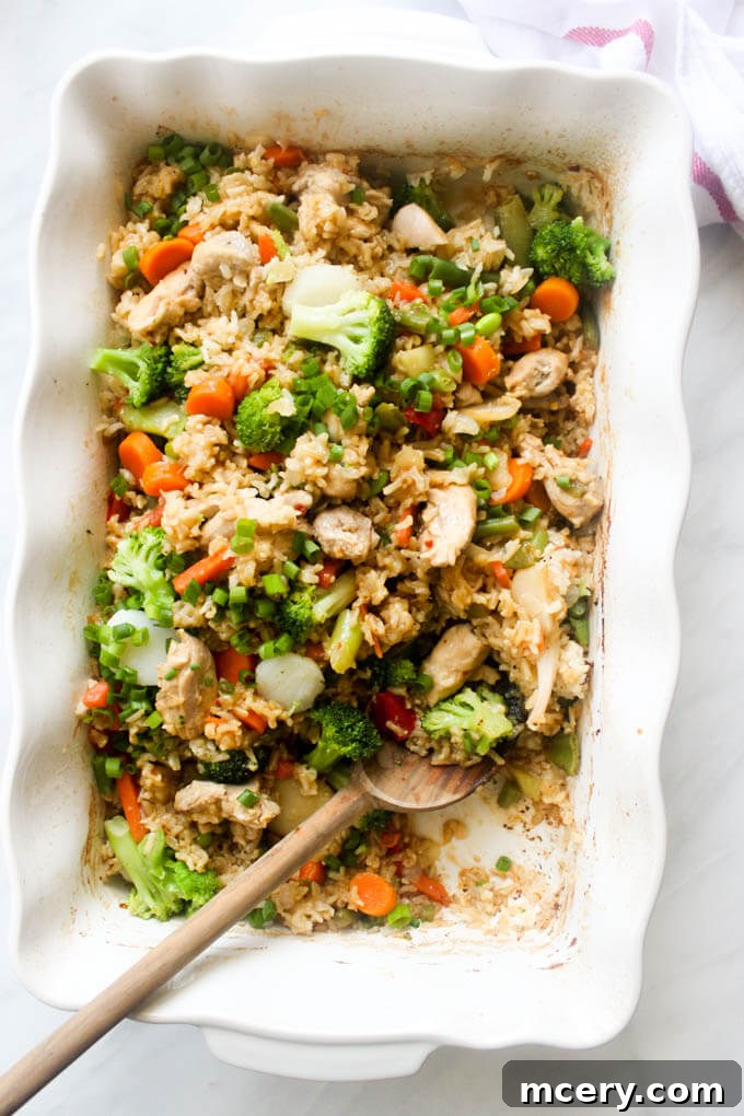 One Pan Teriyaki Chicken and Rice Bake 9 A serving of baked teriyaki chicken and rice in a white casserole dish with a wooden spoon, showcasing the rich sauce and tender chicken.