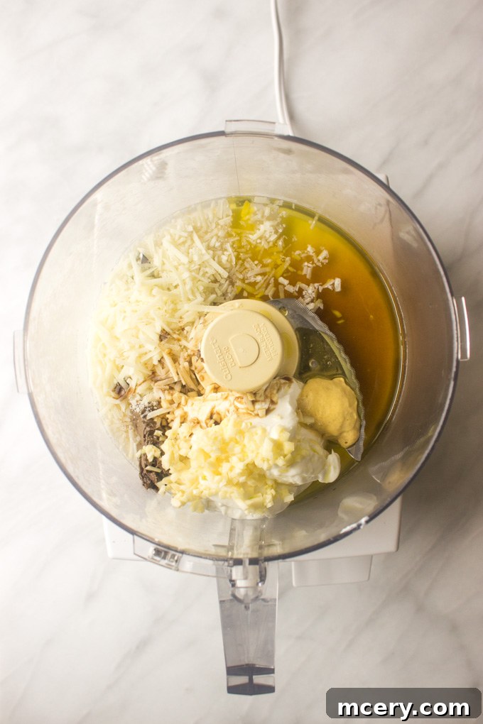 Lush Avocado Caesar 4 All the Greek yogurt Caesar dressing ingredients, including yogurt, anchovies, garlic, lemon, and oil, placed in the bowl of a food processor.