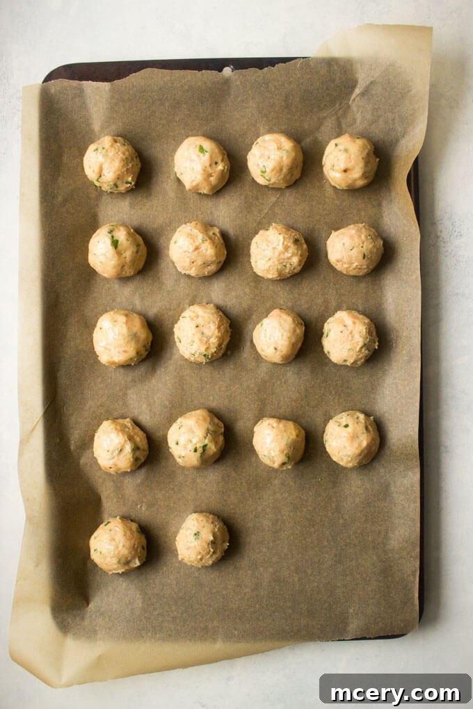 Lean and Flavorful Chicken Meatballs 6 Raw chicken meatballs neatly arranged on a parchment-lined baking sheet, ready for the oven.