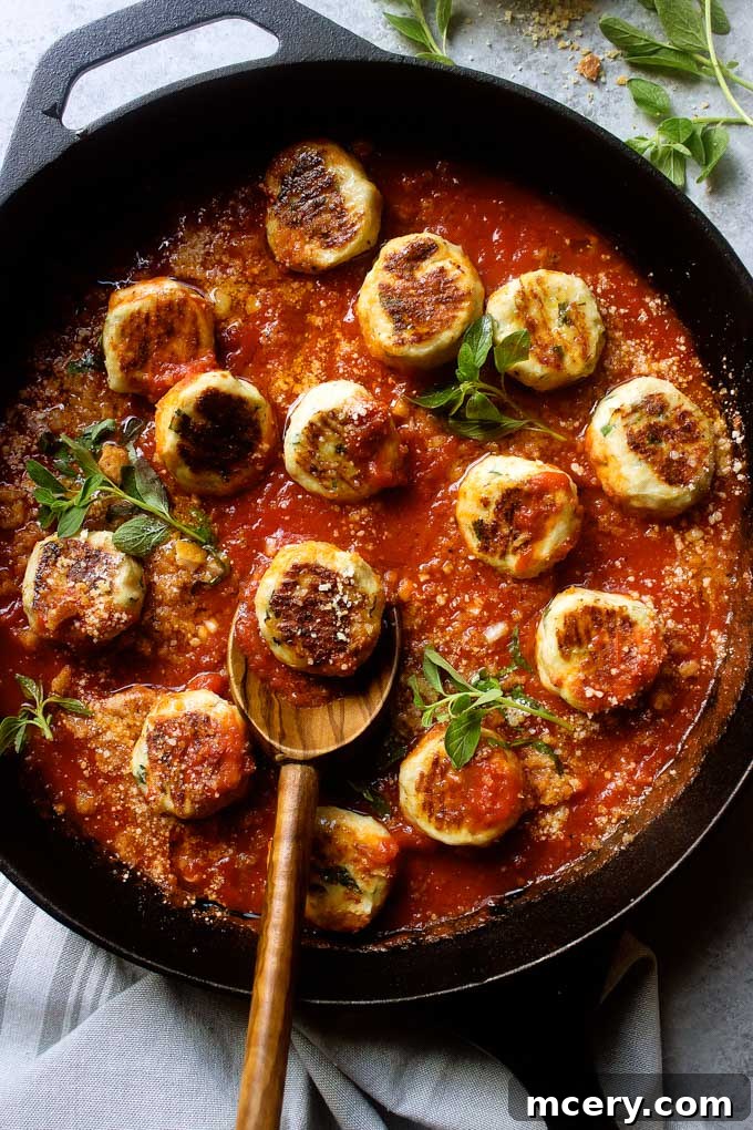 Lean and Flavorful Chicken Meatballs 7 Close-up of baked chicken meatballs submerged in a rich marinara sauce, garnished with fresh basil, in a cast-iron skillet.
