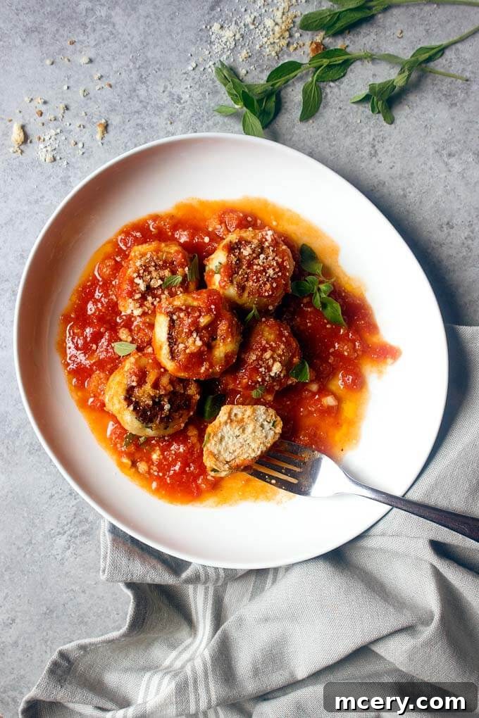 Lean and Flavorful Chicken Meatballs 8 A single healthy chicken meatball on a white plate, with a fork resting beside it, highlighting its tender texture.