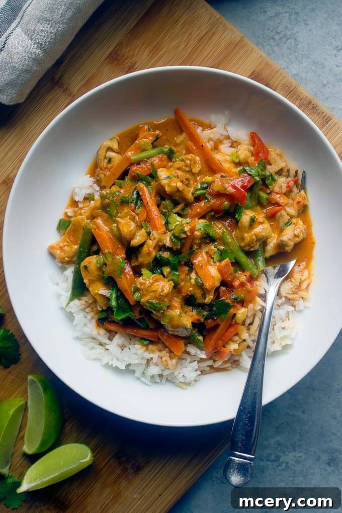 A serving of chicken vegetable curry over white rice in a white bowl, with a fork on the side, highlighting its appetizing presentation