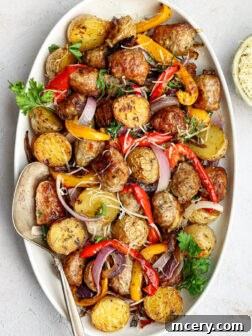 Golden roasted Italian sausage, vibrant bell peppers, sweet red onions, and tender baby potatoes on a white platter.