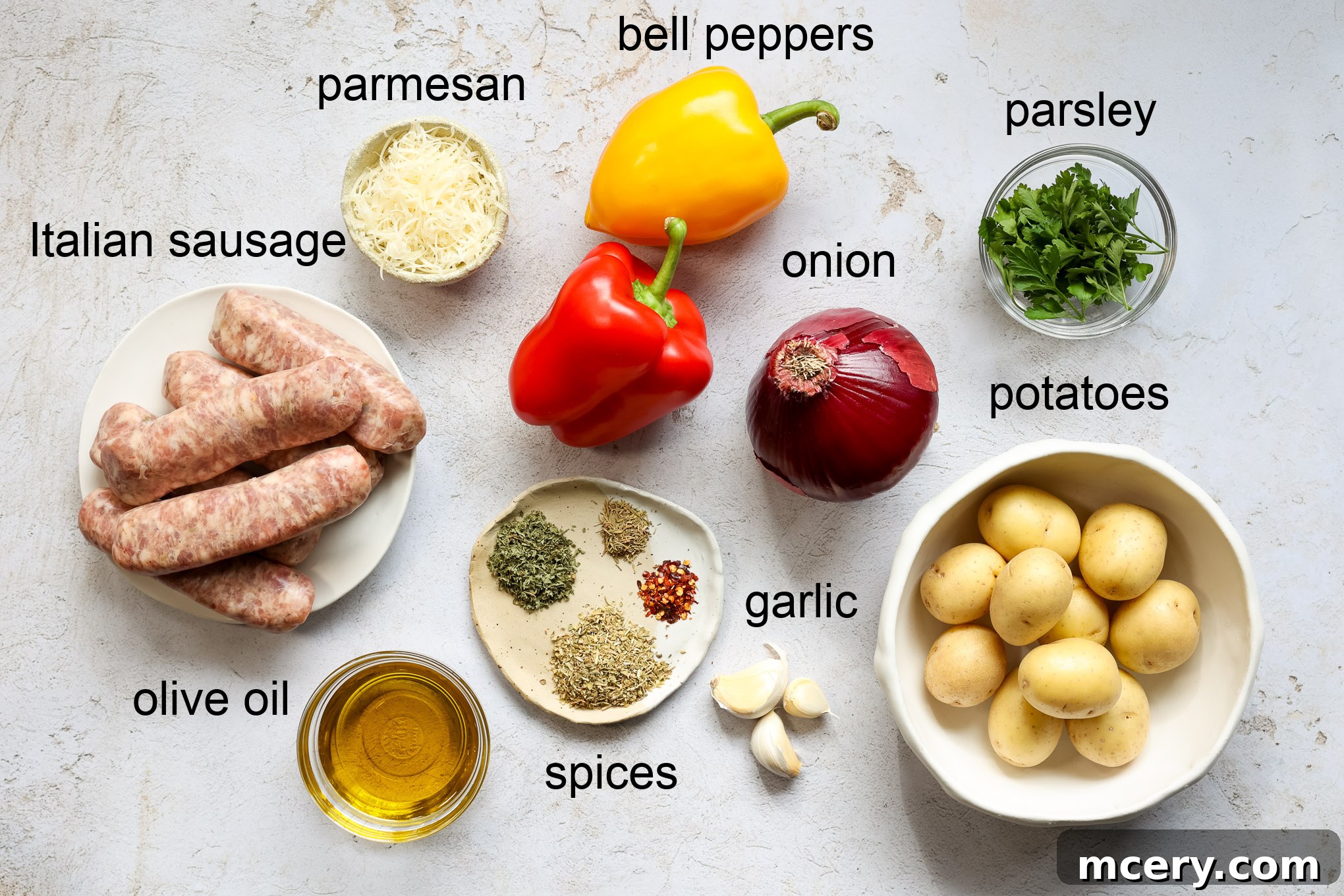 A vibrant selection of fresh ingredients laid out for sheet pan sausage and potatoes, including bell peppers, red onion, baby gold potatoes, Italian sausage, garlic, olive oil, and various dried herbs.