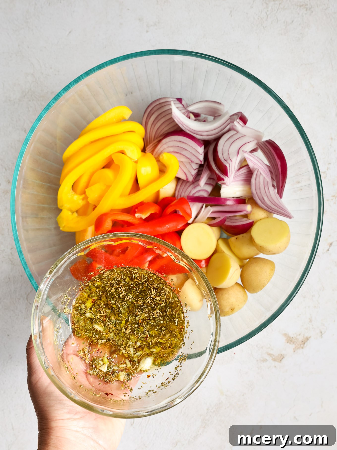 Freshly sliced bell peppers, red onions, and halved baby gold potatoes neatly arranged in a clear glass bowl, ready for seasoning.