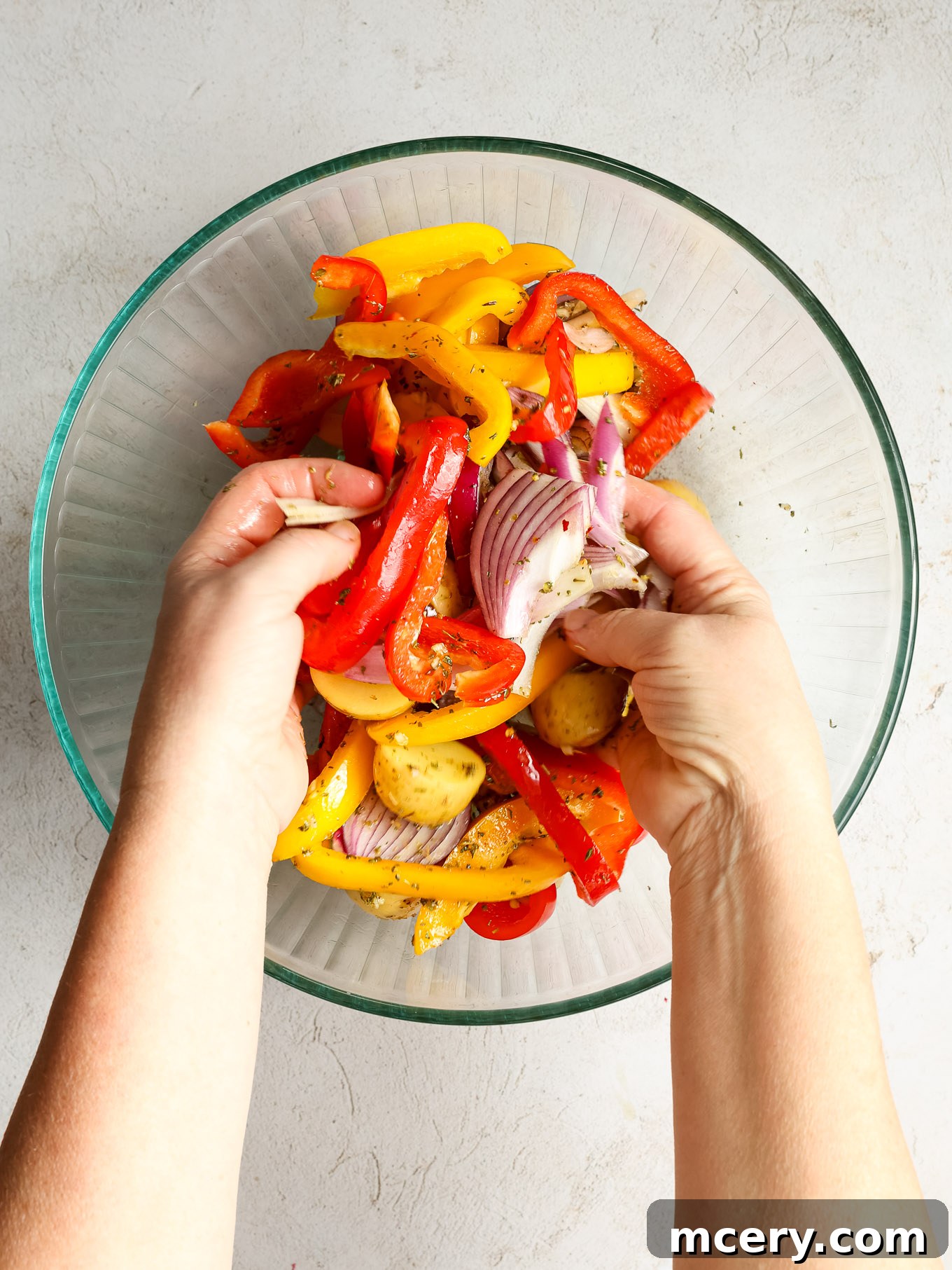 Vibrantly tossed bell peppers, red onions, and baby gold potatoes glistening with a savory herb oil mixture in a glass bowl.