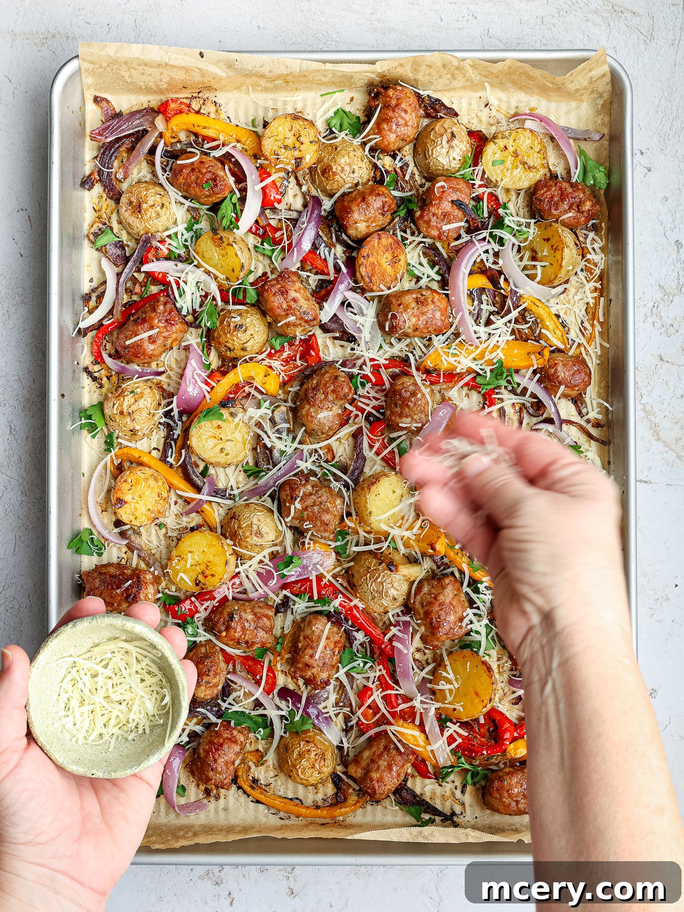 Perfectly roasted Italian sausage and tender baby potatoes served on a sheet pan, generously garnished with freshly grated Parmesan cheese and green parsley.