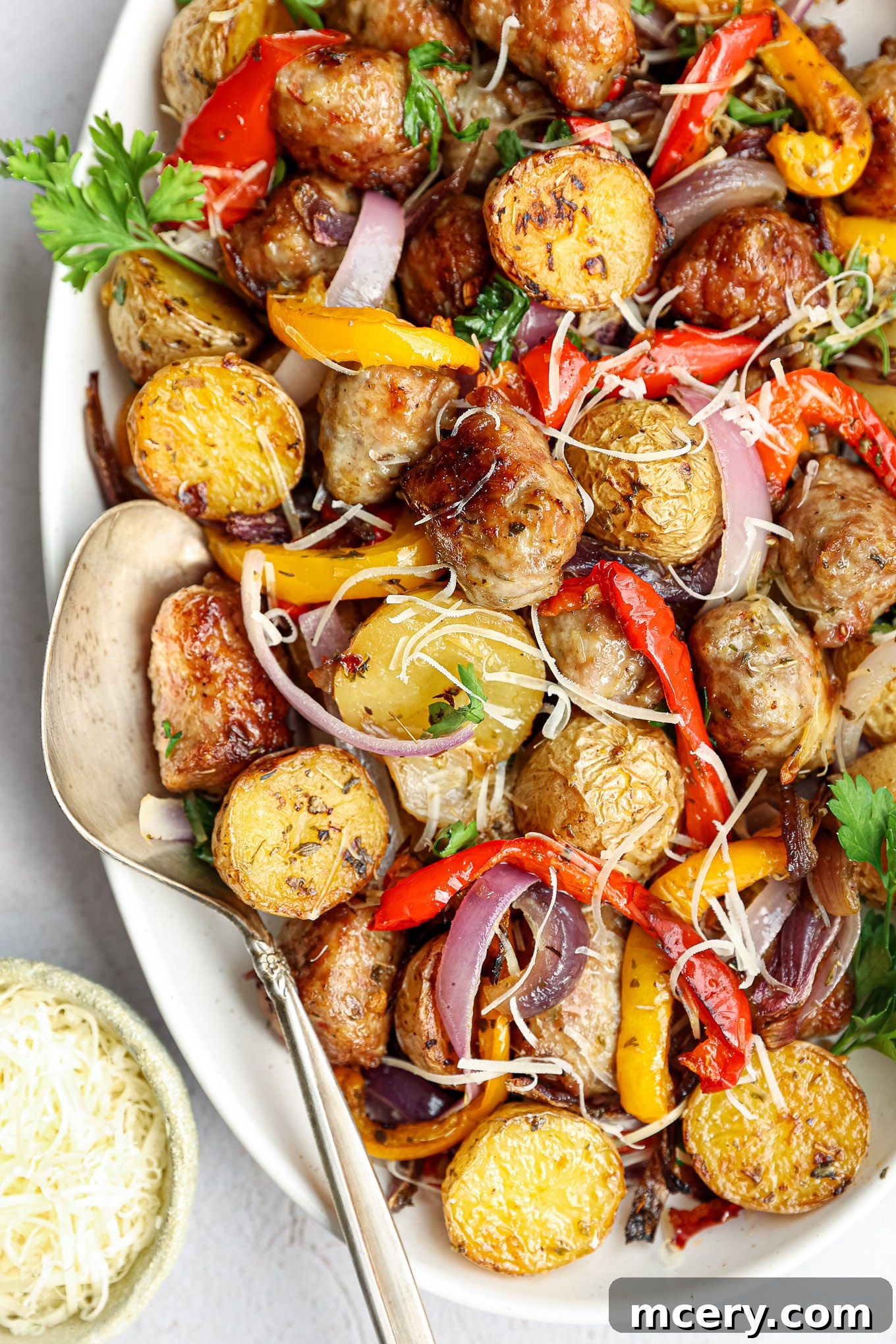 Close-up shot of perfectly roasted Italian sausage and tender baby potatoes with a serving spoon on the side, ready to be enjoyed.