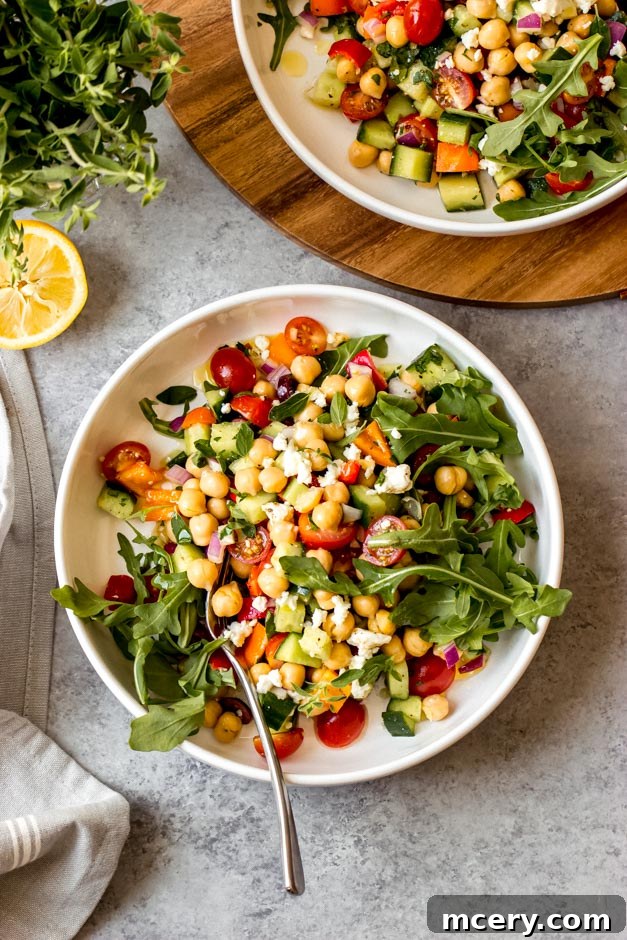 Vibrant Mediterranean Chickpea Salad 2 Vibrant Greek Chickpea Salad with a refreshing honey lemon dressing, presented in a white bowl on a gray background, showcasing its fresh ingredients for a healthy and easy meal.