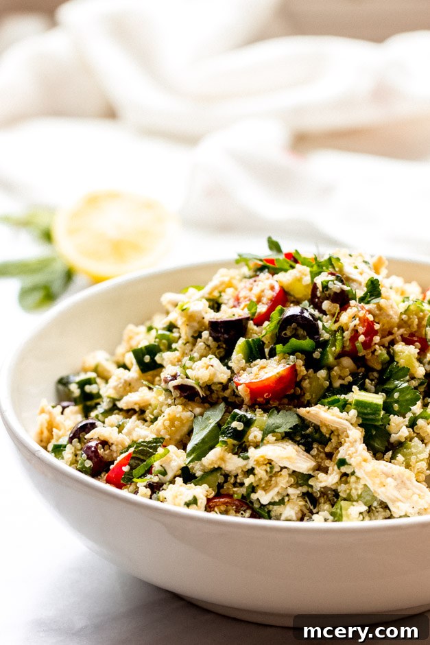 Vibrant Lemon Chicken Quinoa Bowl 7 Close up side view of a generous portion of lemon chicken quinoa salad in a white bowl, showing layers of quinoa, chicken, and colorful vegetables.