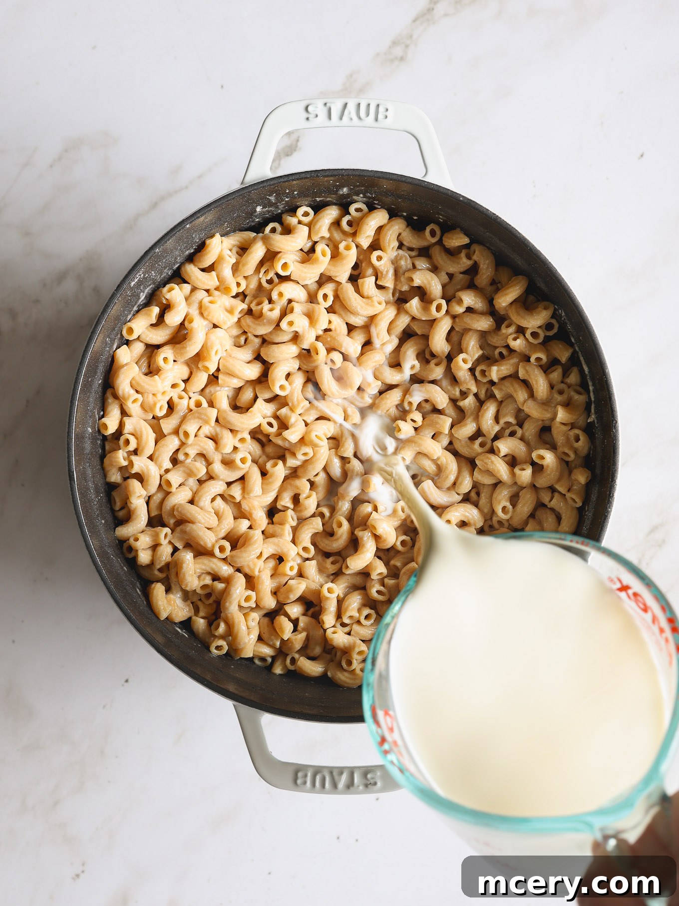 Guilt Free Whole Wheat Mac and Cheese 6 Milk and ground mustard being added to whole wheat macaroni in a Dutch oven, simmering to thicken.