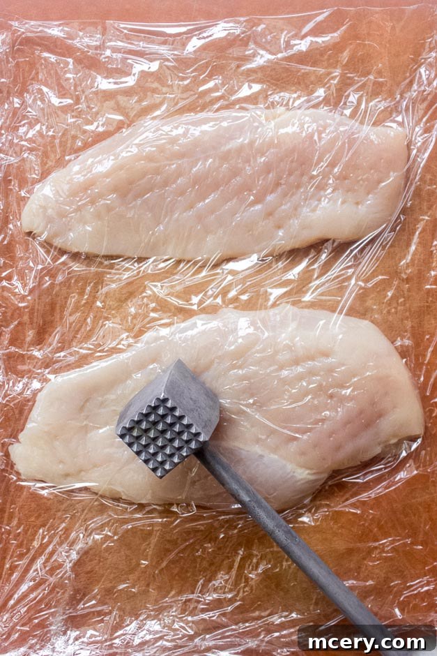 Creamy Coconut Chicken Skillet 4 Chicken breast being pounded between plastic wrap to an even thickness.