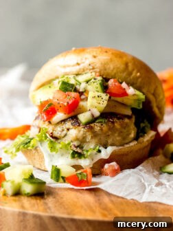 Close up straight view grilled turkey burger with fresh lettuce, tomato, and tzatziki