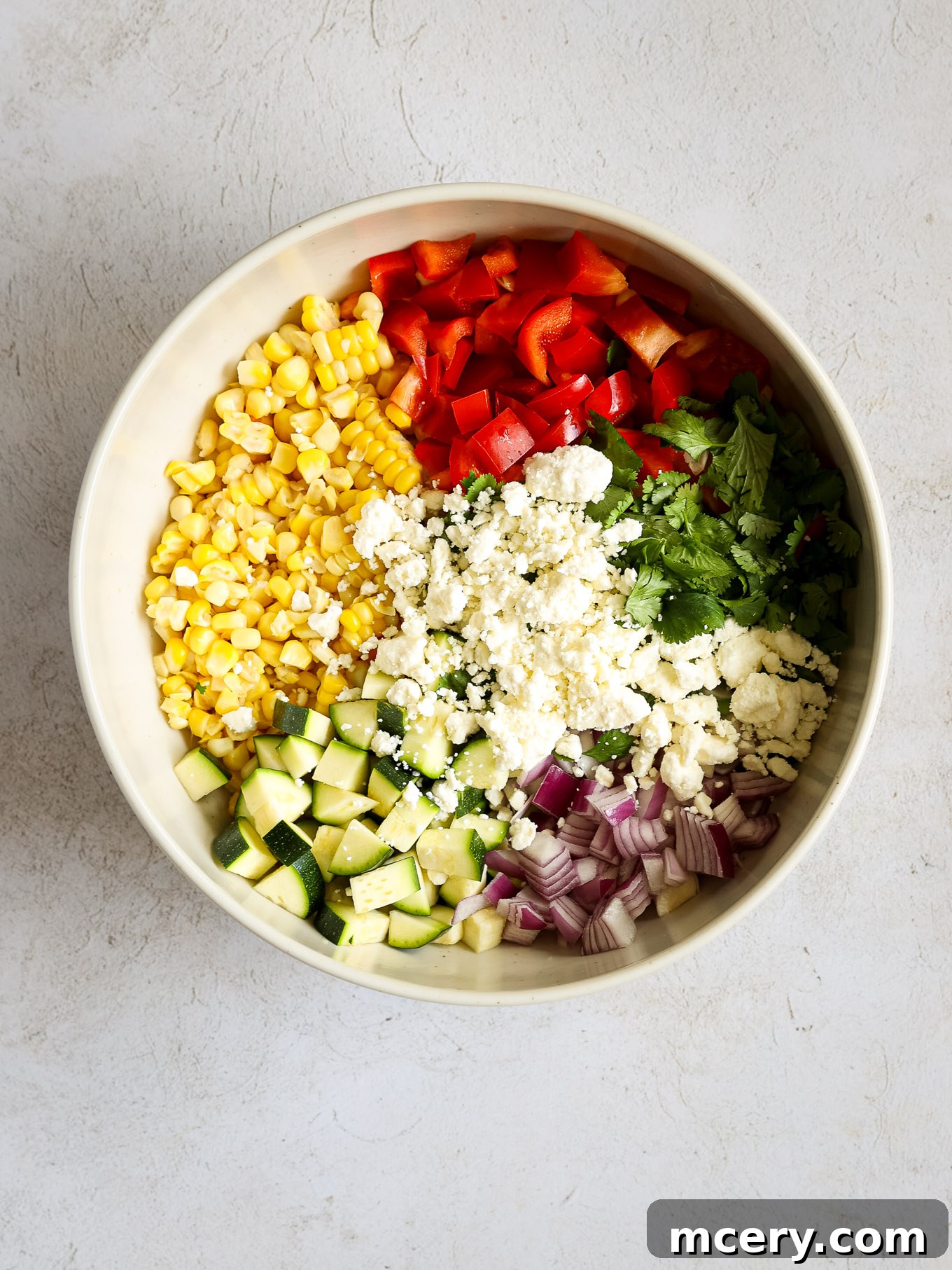 Vibrant Zucchini Corn Medley 4 Finely chopped vegetables (corn, bell pepper, zucchini, red onion, cilantro, feta) ready in a large mixing bowl.