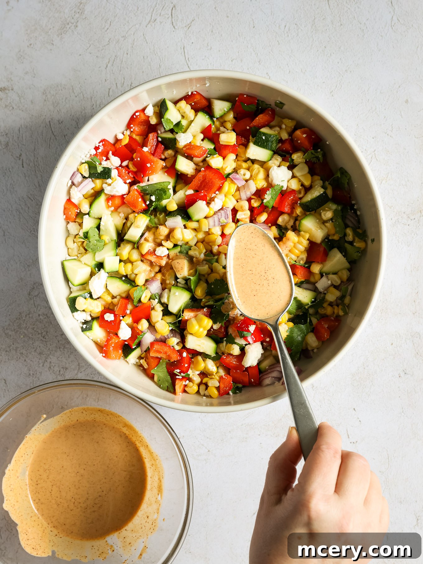 Vibrant Zucchini Corn Medley 6 Salad vegetables in a bowl with creamy dressing being poured over them.