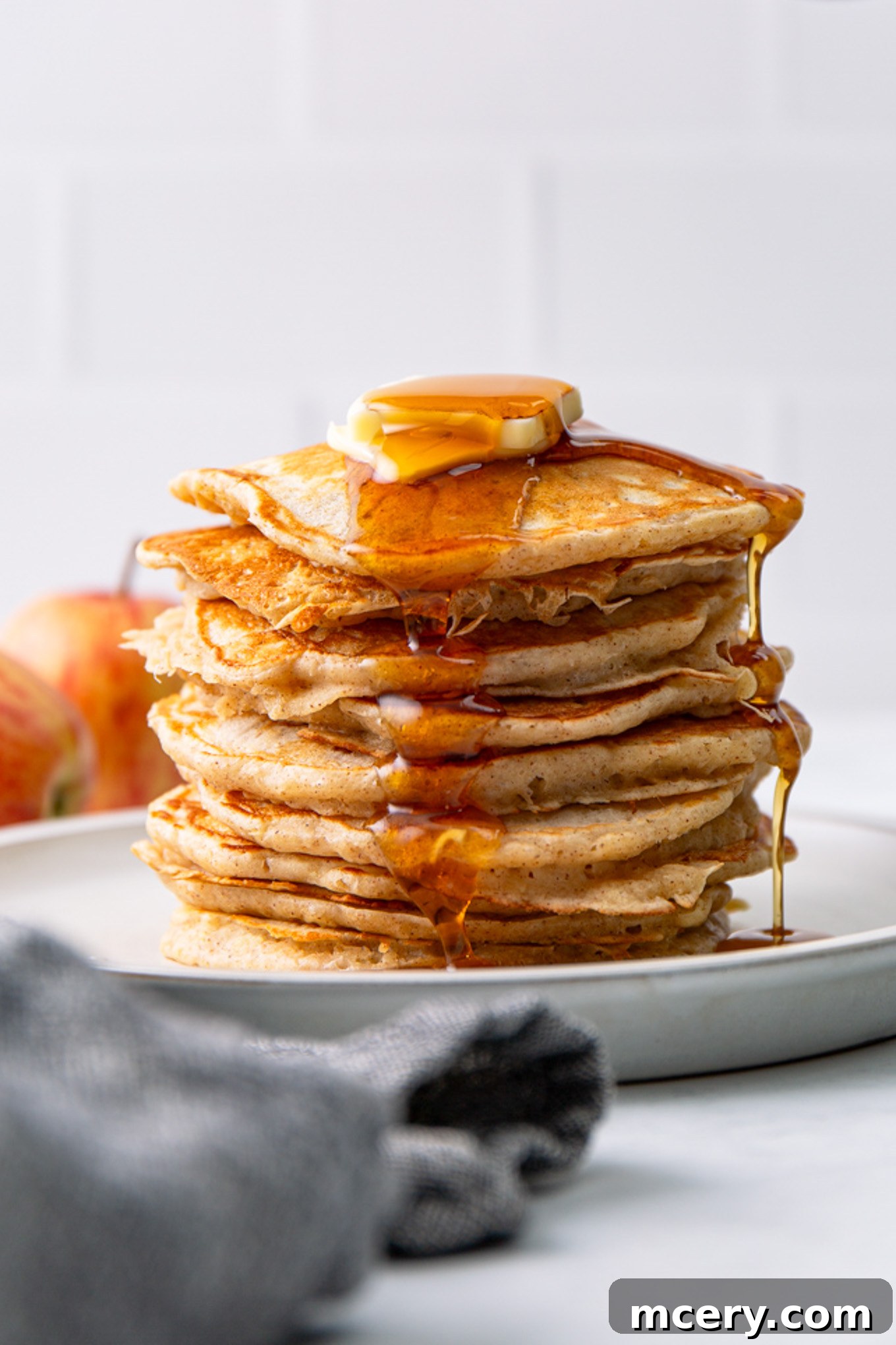 Stacked apple cinnamon pancakes drizzled with syrup and topped with a pat of butter, ready to be enjoyed as a delightful breakfast.