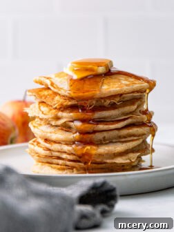 Stacked apple cinnamon pancakes with syrup and butter for a delicious breakfast.