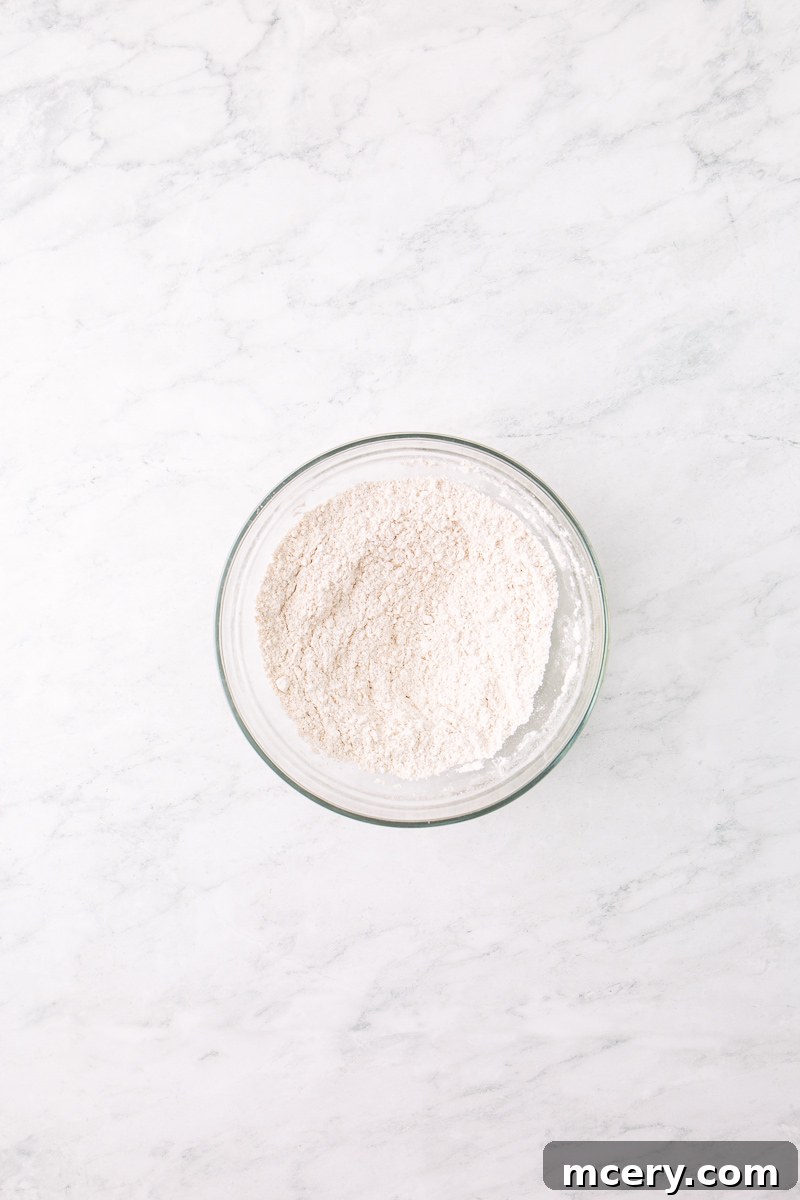 Dry ingredients for pancakes in a clear glass bowl, including flour, sugar, baking powder, cinnamon, and salt, ready to be whisked.