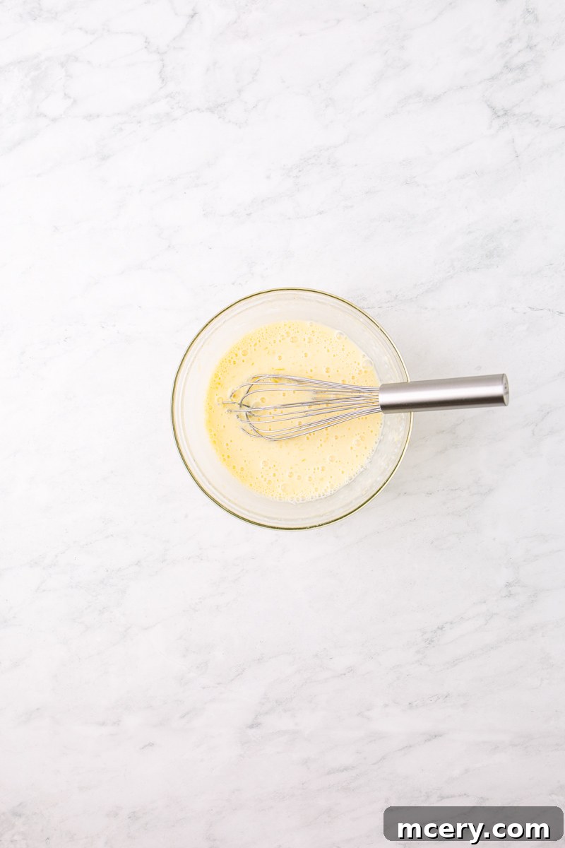 Wet ingredients for pancakes in a separate glass bowl, including buttermilk, a cracked egg, melted butter, and vanilla extract, ready to be whisked.