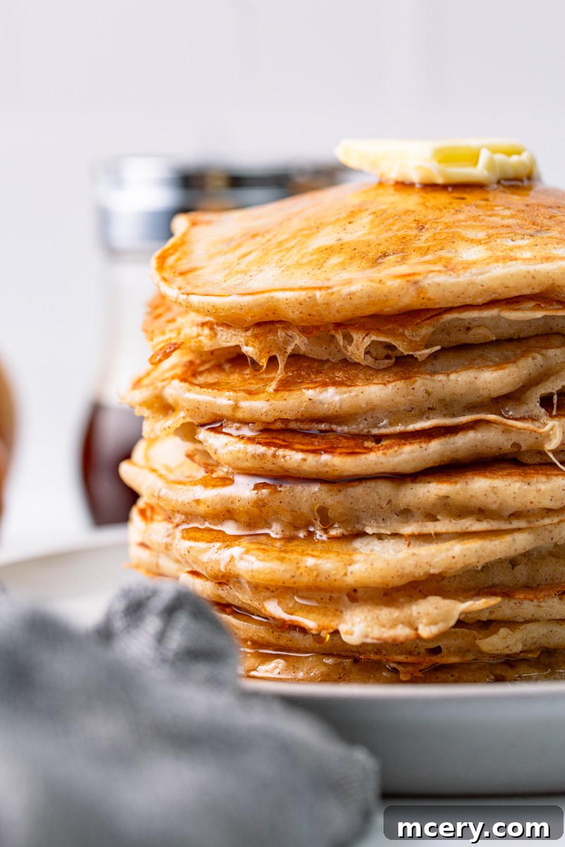 Close-up of a stack of golden brown apple cinnamon pancakes, generously topped with syrup, showcasing their fluffy texture.