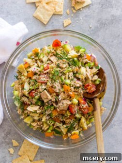 Overhead view of a Greek tuna salad in a bowl, garnished with herbs.