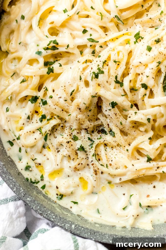 A bowl of garlic Parmesan cream sauce with a spoon, showing its creamy texture, garnished with fresh parsley.