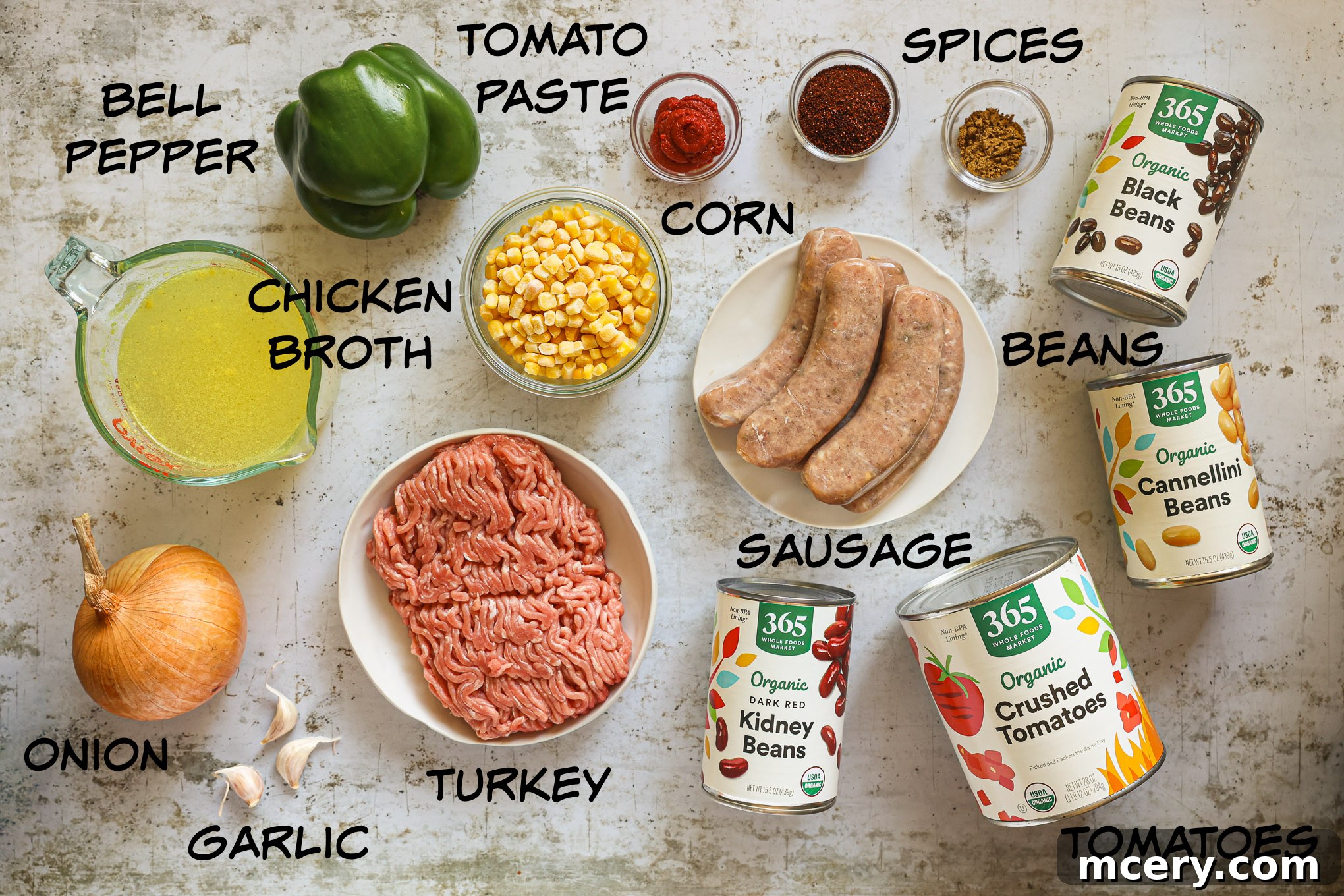 Hearty Three Bean Turkey Chili 3 A colorful array of ingredients for turkey bean chili, including canned beans, ground turkey, vegetables, and spices, arranged on a rustic wooden surface.