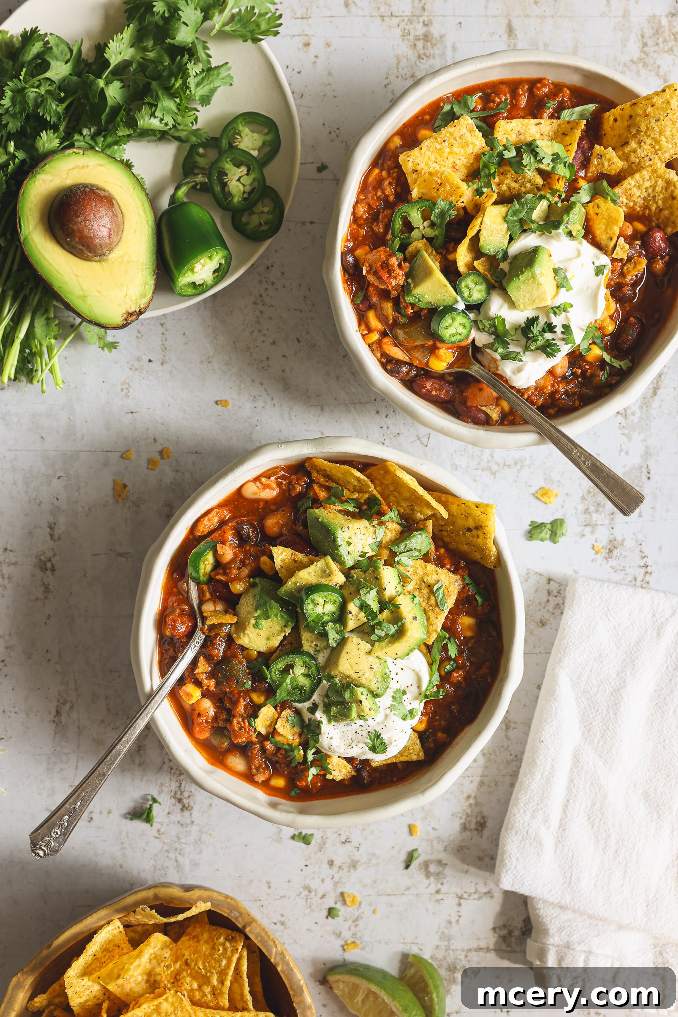 Hearty Three Bean Turkey Chili 8 A beautifully presented bowl of three-bean turkey chili, garnished generously with fresh avocado slices and cilantro, highlighting its appealing texture and vibrant toppings.