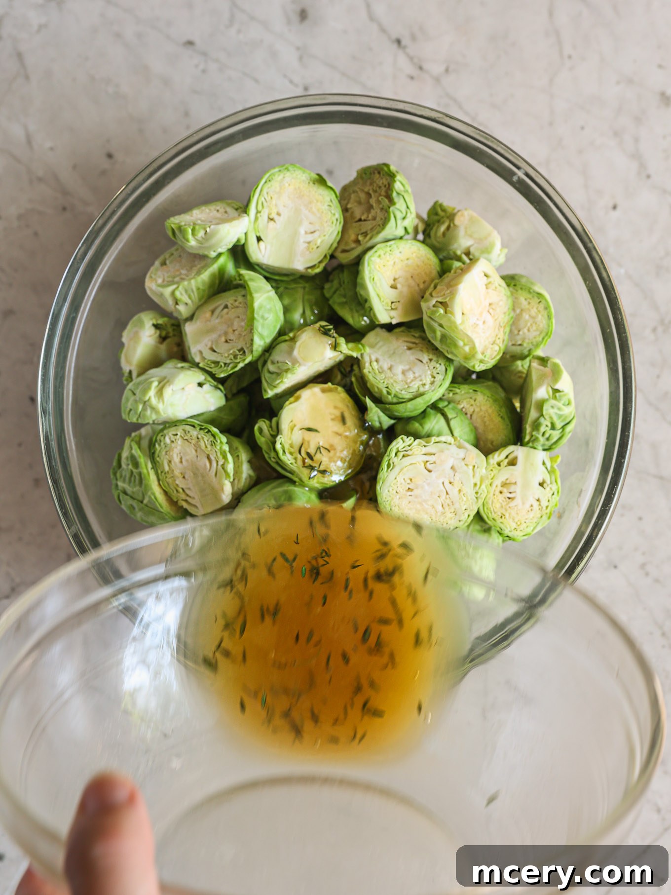 Halved Brussels sprouts glistening with the maple butter mixture in a large glass bowl, pre-seasoned with salt and pepper.