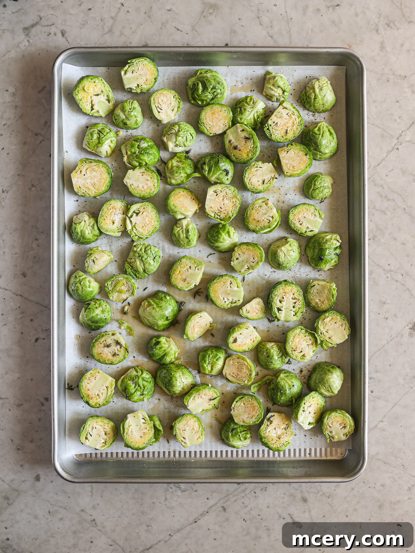 Raw, halved Brussels sprouts arranged in a single, even layer on a parchment-lined baking sheet, ready for roasting.