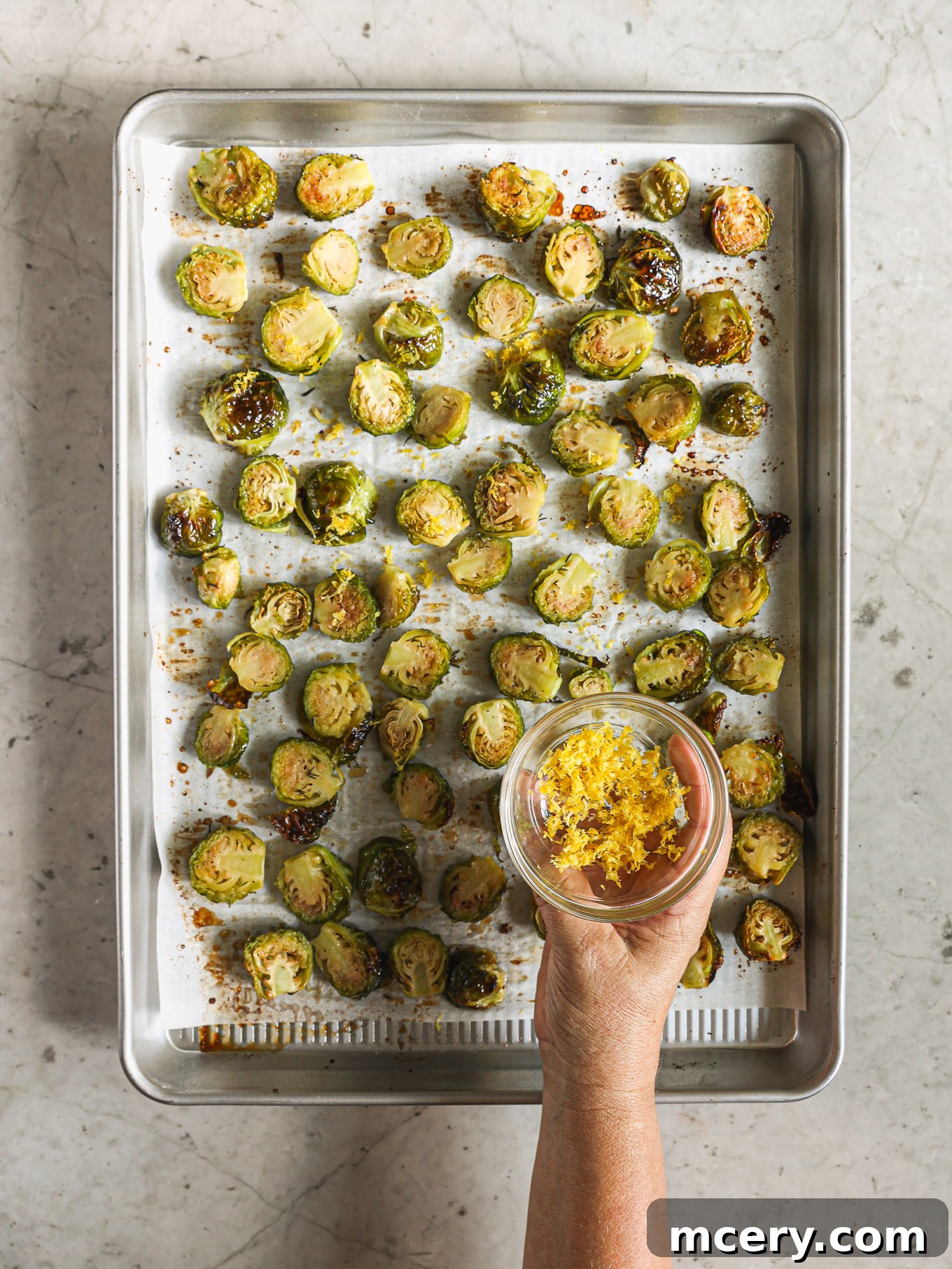 Freshly roasted Brussels sprouts sprinkled with bright yellow lemon zest, still on the baking sheet, awaiting a final toss.