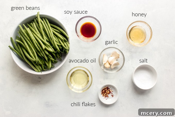Sesame Garlic Green Beans 3 Fresh ingredients for making spicy Asian green beans including green beans, garlic, soy sauce, and honey arranged on a cutting board.