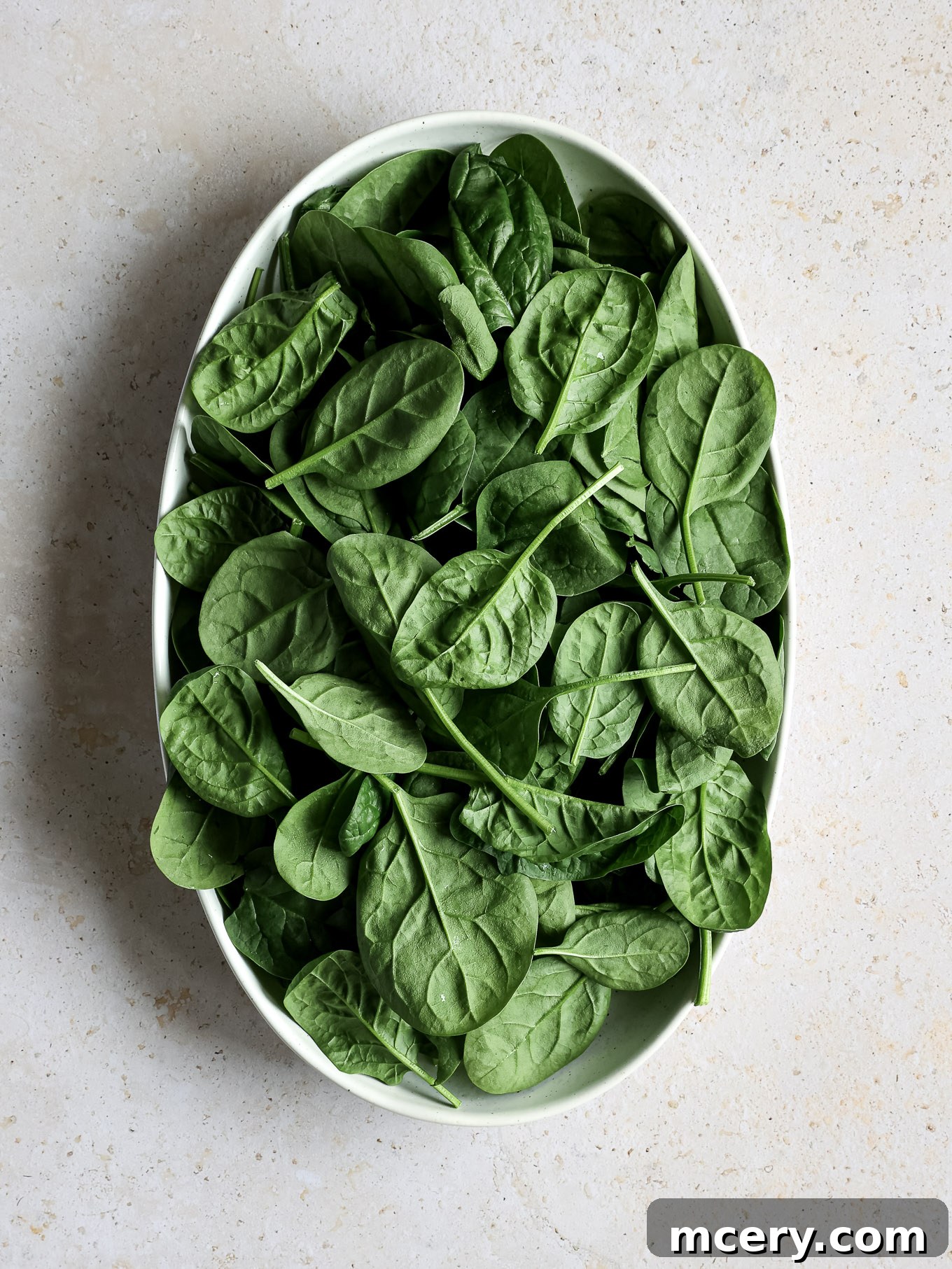 Vibrant Strawberry Chicken Salad 3 Fresh baby spinach leaves are gently placed into a large wide bowl, forming the base of the salad.