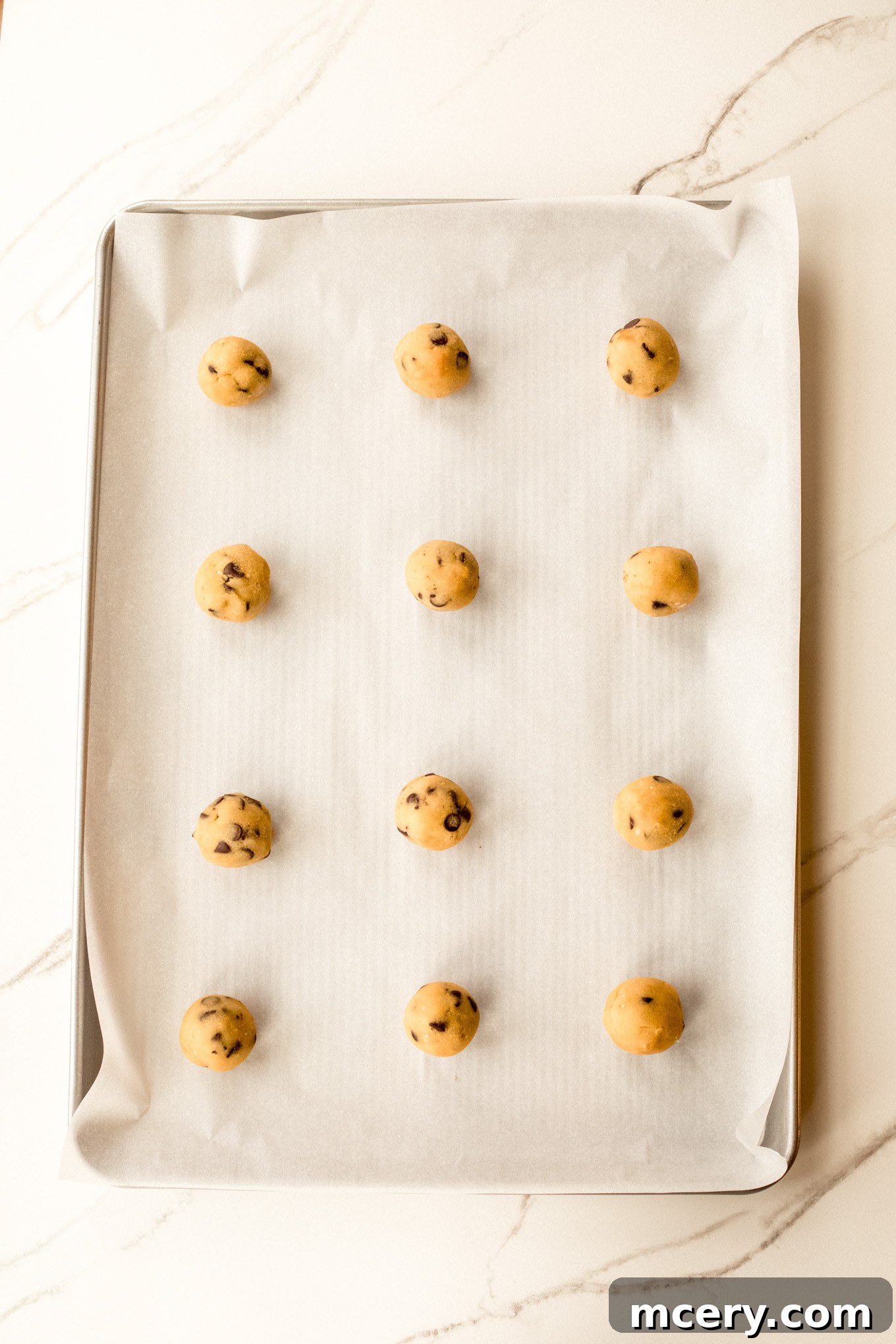 Scoops of chilled cookie dough, rolled into even balls, placed on a baking sheet lined with parchment paper, spaced for even baking.