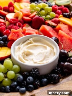 A bowl of creamy fruit dip, garnished with a few fresh berries, and surrounded by an assortment of colorful fruits ready for dipping.