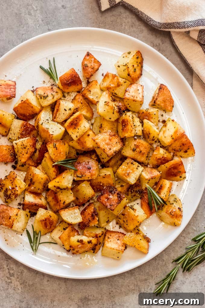 Crispy Rosemary Roasted Potatoes 2 rosemary garlic potatoes on a white plate, garnished with fresh rosemary sprigs.