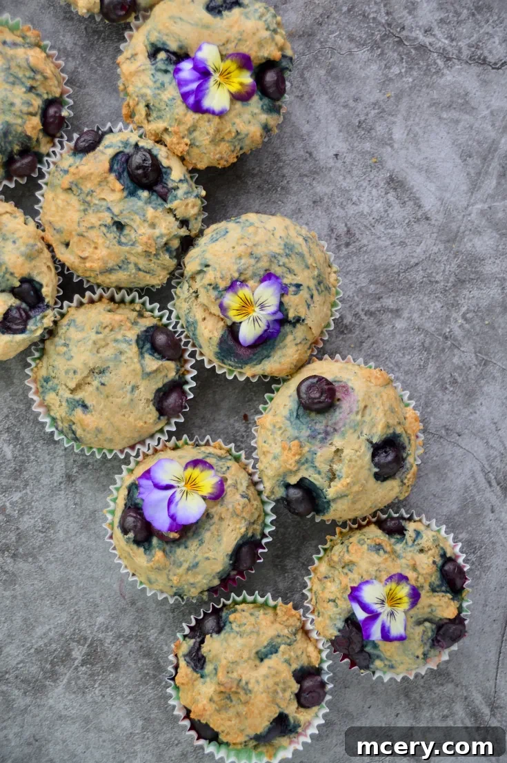 Beautifully arranged vegan blueberry muffins with scattered purple and yellow flower petals, showcasing their golden tops and visible blueberries.