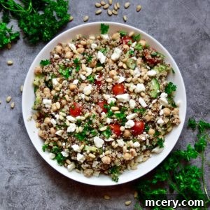 A bowl of Mediterranean Quinoa Salad with pine nuts, parsley, cherry tomatoes, feta cheese, and cucumber on a gray surface.