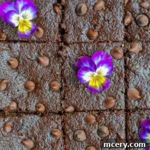 Irresistibly Fudgy Gluten-Free Brownies 2 A tray of sliced Fudgy Gluten-Free Brownies topped with chocolate chips and decorated with purple and yellow edible flowers.