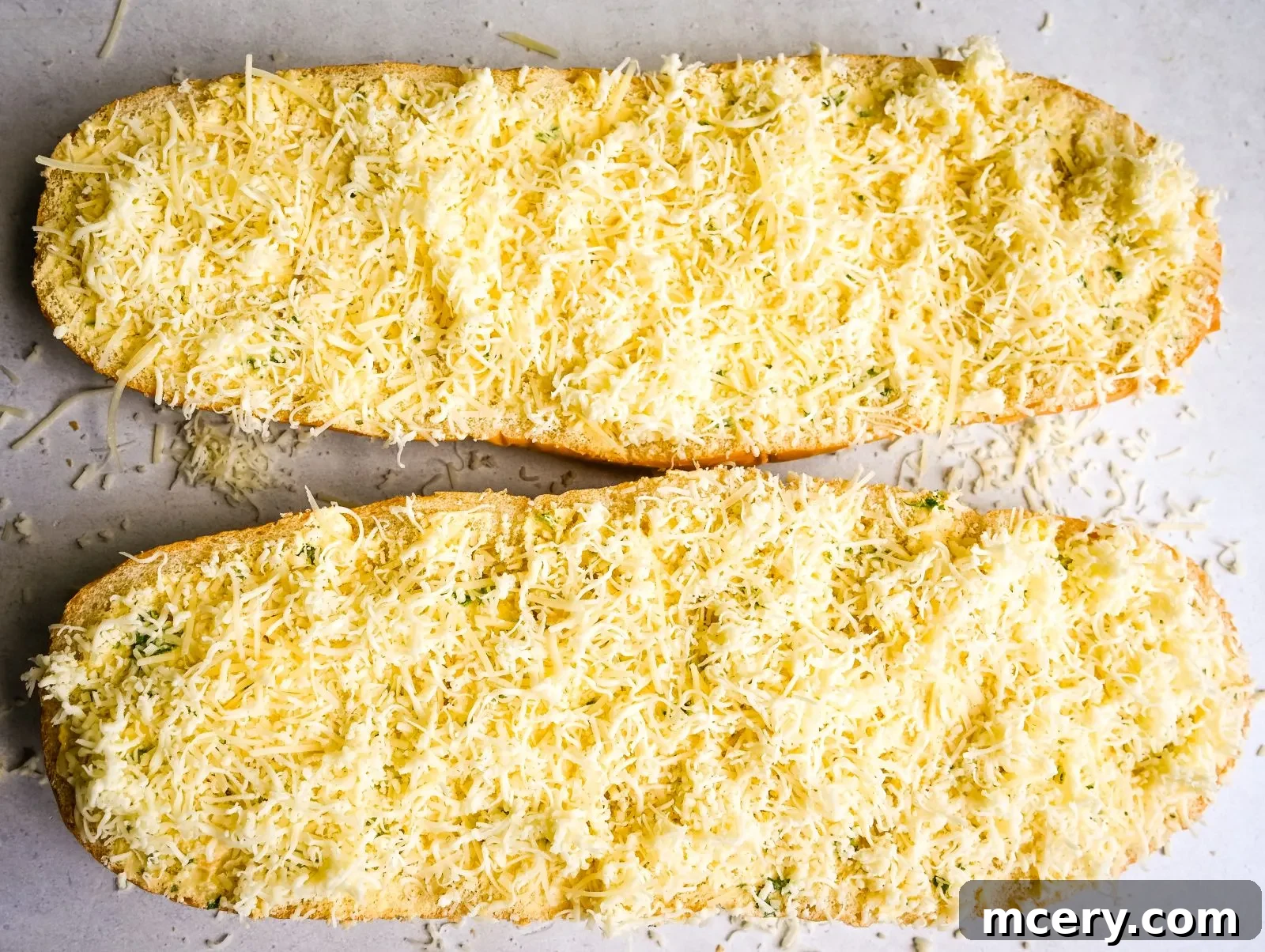 Sliced cheesy garlic bread on a white platter with a few fresh parsley sprigs. The bread pieces are arranged invitingly, showcasing their toasted edges and the bubbly, melted cheese topping. Some crumbs are scattered around the platter, indicating the bread's crisp texture.