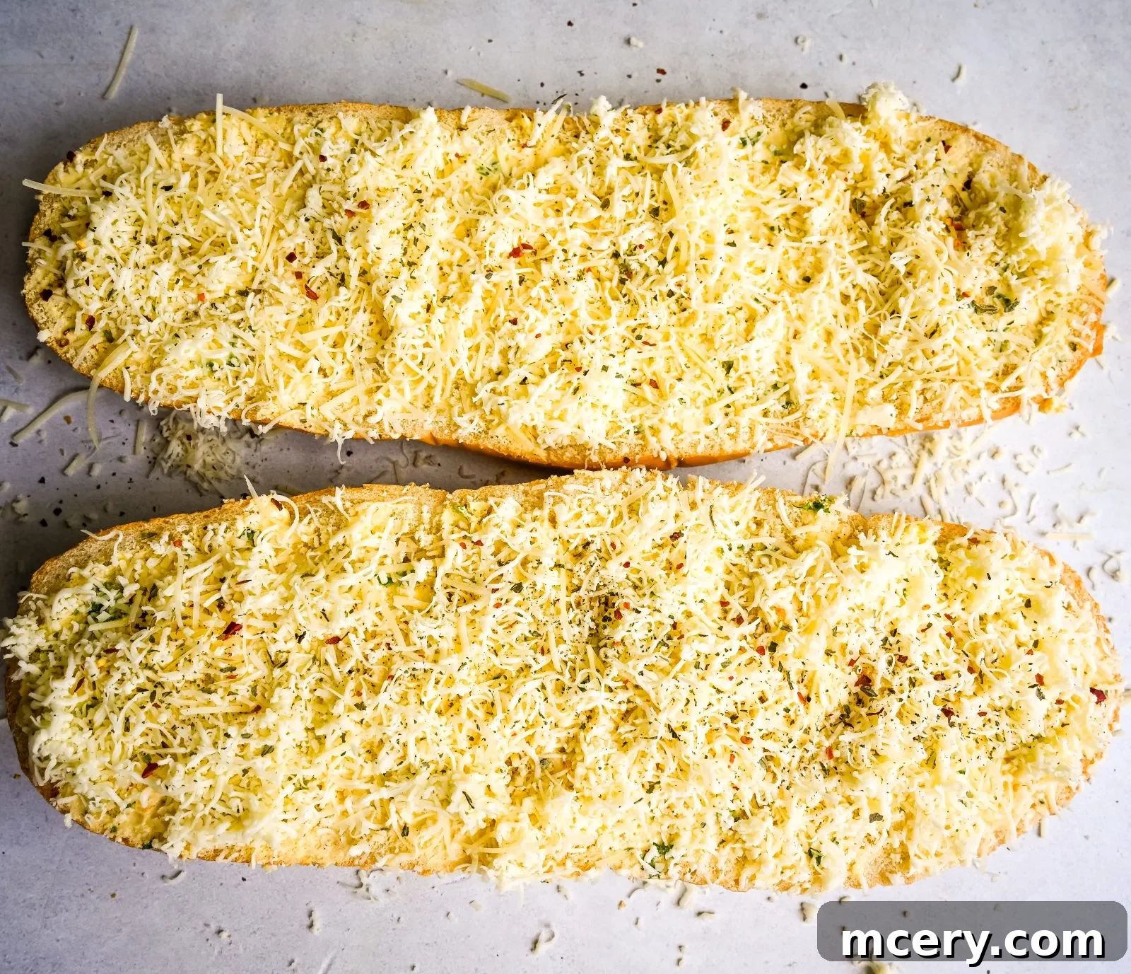 A close-up of a single slice of cheesy garlic bread, held up against a blurred background. The slice is perfectly toasted with golden-brown crusts, and the melted cheese stretches invitingly. Green herbs are sprinkled on top, adding a fresh visual element.