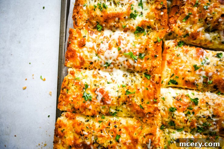 Close-up of slices of cheesy garlic bread topped with melted cheese and garnished with chopped parsley. The bread has a golden-brown crust, and some crumbs are visible on the white paper background, highlighting the texture and freshness of the slices.