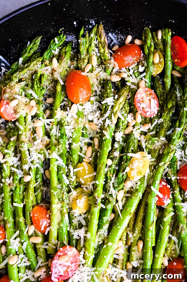 A skillet filled with vibrant Lemon Garlic Asparagus, topped with halved cherry tomatoes, grated cheese, and pine nuts. Lemon slices are arranged on the side, adding a fresh touch to the dish. The image showcases a colorful and healthy vegetable medley.