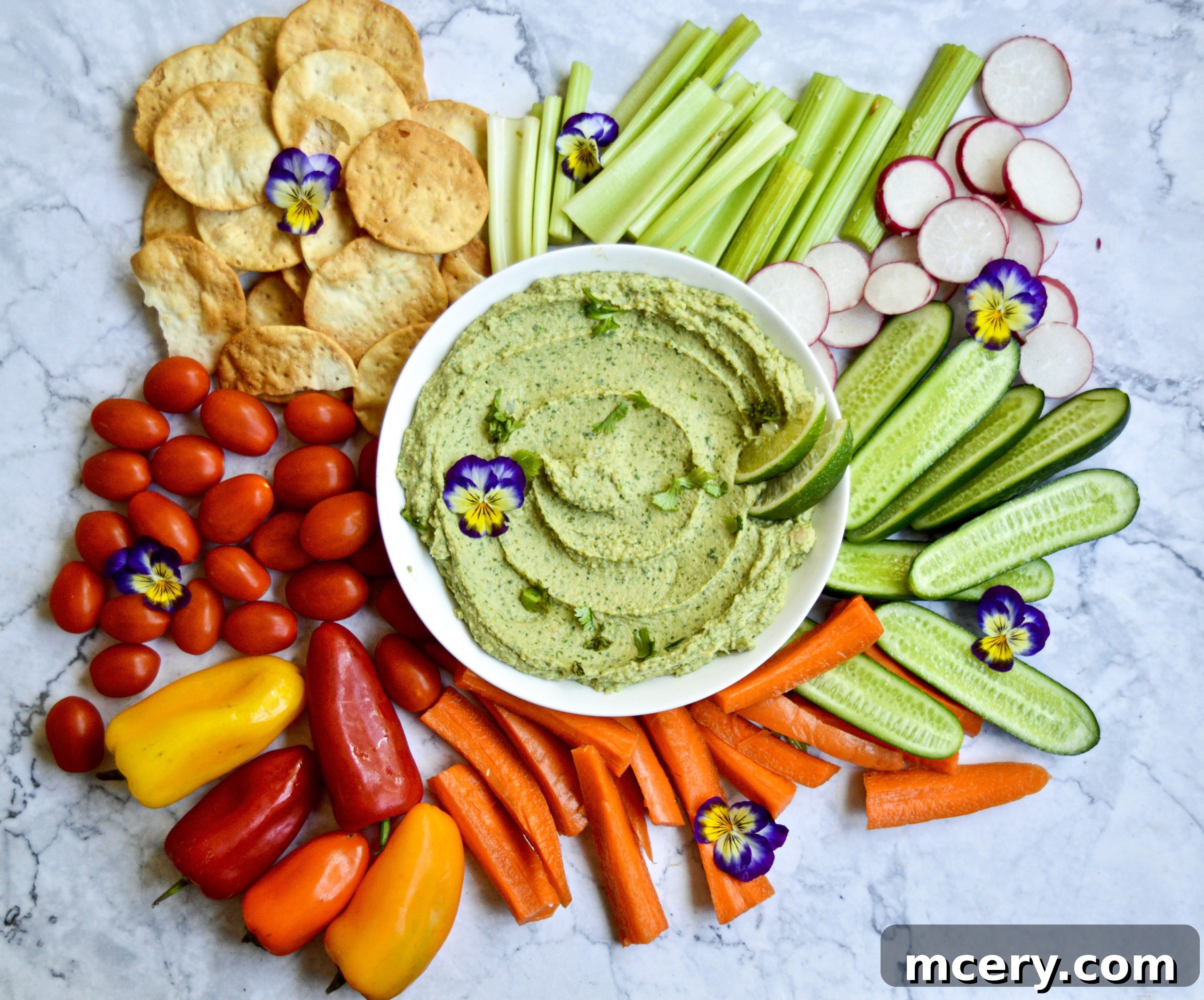 Zesty Cilantro Jalapeño Hummus 2 A vibrant bowl of cilantro jalapeño hummus with fresh cilantro and lime wedges, surrounded by colorful vegetable sticks and pita chips, inviting a healthy snack.